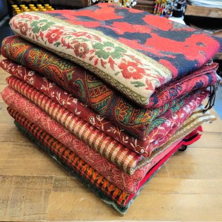 Stack of colorful 100% acrylic multi-pattern wool scarves in reds greens and golds ideal for summer evenings