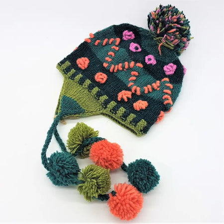 A dark green and teal wool bobble hat with pom-pom tassels and textured floral embroidery for kids and small adults
