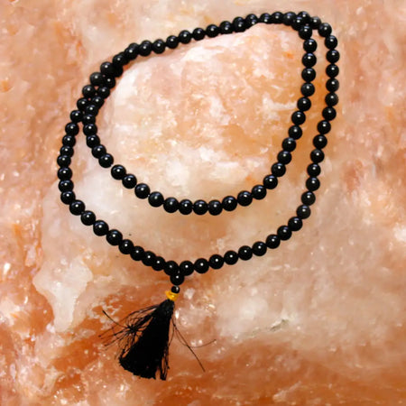 Black agate mala necklace with 108 beads and a black tassel shown alongside a velvet pouch