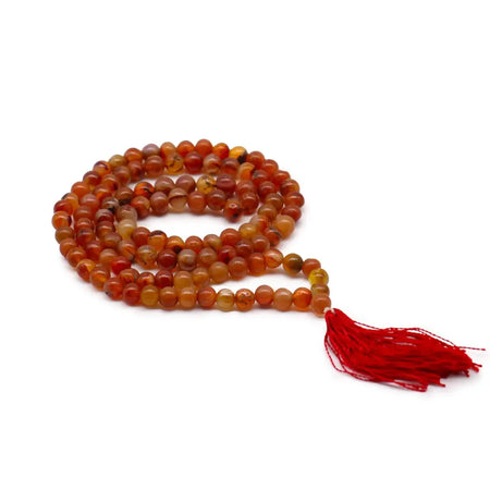 A coiled 108 bead mala necklace with warm amber carnelian beads and a vibrant red tassel, shown with a velvet pouch