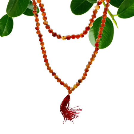 A double-strand amber carnelian bead mala necklace with a vibrant red tassel and a velvet pouch background