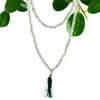 A 108 bead mala necklace made of white jade with a dark green aventurine tassel and a velvet pouch background