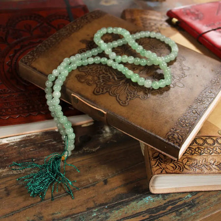A light green green aventurine mala necklace with 108 beads and a teal tassel shown with a velvet pouch