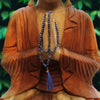 A deep blue lapis lapis lazuli bead mala necklace with matching tassel draped on a wooden buddha statue next to a velvet pouch