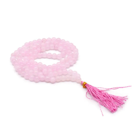 A delicate pink rose quartz bead mala necklace with 108 beads and a matching tassel beside a velvet pouch