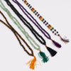 A collection of mala necklaces with tiger eye beads in various colors and materials each with a tassel and velvet pouch