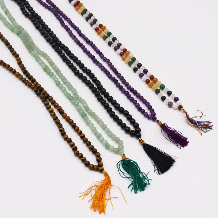 A collection of mala necklaces with tiger eye beads in various colors and materials each with a tassel and velvet pouch