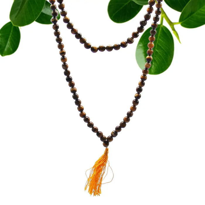 A brown tiger eye mala necklace with 108 beads and a golden tassel shown with a velvet pouch