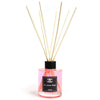 A pink glass bottle reed diffuser with black cap and light wooden reeds labeled jasmine wings