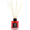 A vibrant red glass bottle reed diffuser with black cap and light wooden reeds for pomegranate and nutmeg scent