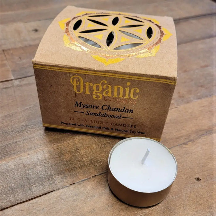 A white tea light candle in a gold tin next to india organic sandalwood packaging with six fragrances options