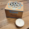 A white tea light candle in a gold metal cup beside a brown box with blue and gold designs for india organic scented tealights