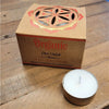 A white organic scented tealight candle in a metal tin beside its brown box with india organic red and gold design