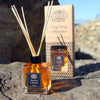 Square glass reed diffuser with amber rose essential oil and eco-mineral oil base surrounded by light brown rattan sticks