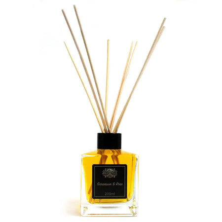 Clear glass square bottle with black cap filled with golden yellow rose essential oil and rattan sticks diffuser