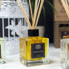 A square glass reed diffuser bottle with golden-yellow rose essential oil and eco-mineral oil base by aromatics