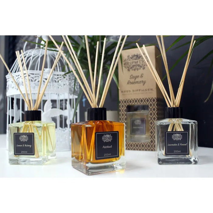 Three square glass reed diffusers with wooden reeds filled with lemon nutmeg yellow amber patchouli and clear lavender fennel oils