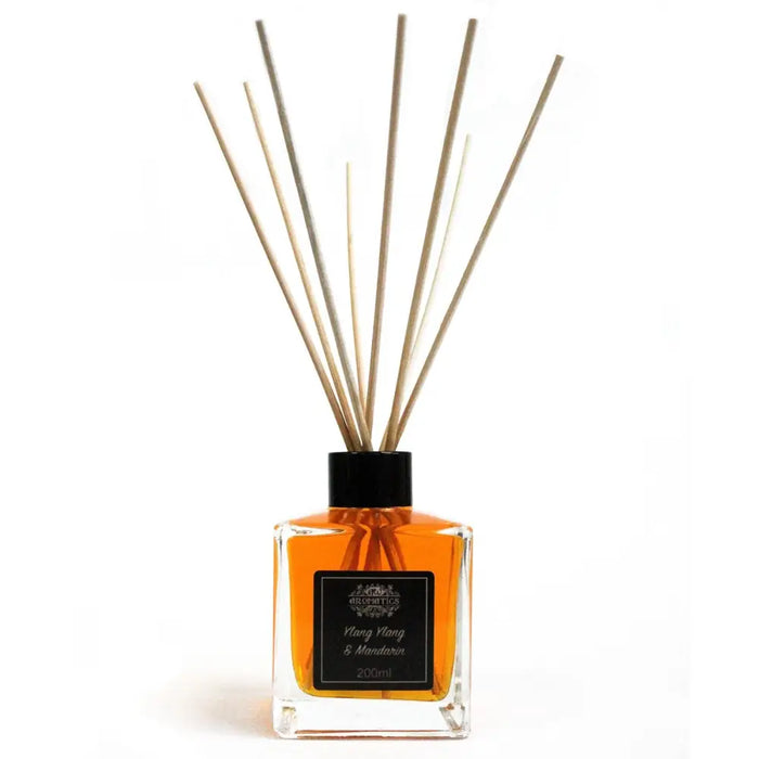 Clear glass reed diffuser with black cap filled with amber mandarin essential oil and wooden reeds of ylang ylang scent
