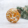 A clear glass 3 inch amber botanical bauble filled with dried orange petals and topped with a bronze metal cap