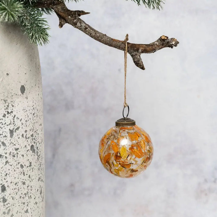 A 3 inch amber botanical bauble with orange and yellow dried leaves hanging from rustic branch twine loop