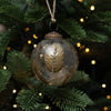 A clear glass 3 inch leaf botanical bauble with a gold leaf design and brass cap hanging from natural twine