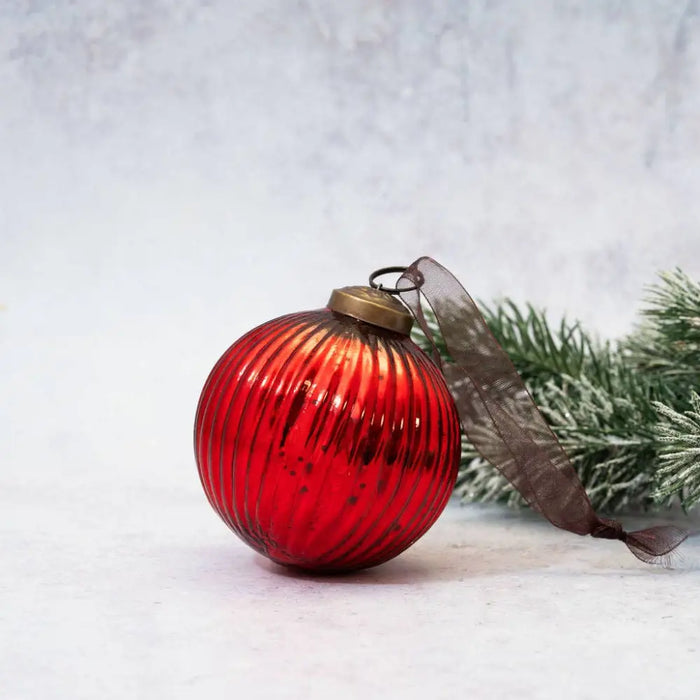 A 3 inch red glass ball decoration with vertical ridges and a brass cap tied with a sheer brown ribbon