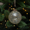 A clear glass 3 inch spray botanical bauble with dried flowers and branches hanging from rustic twine loop