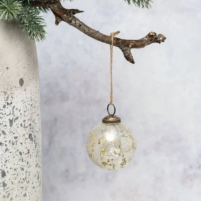 A clear 3 inch glass spray botanical bauble with gold leaf floral patterns hanging by natural twine loop and metal cap