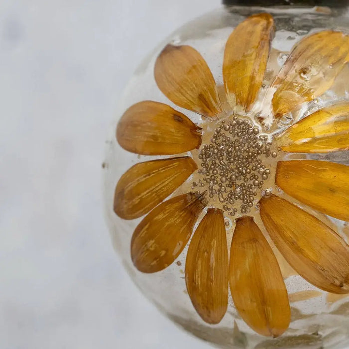 A 3 inch zinnea botanical bauble with a clear glass ornament holding a preserved yellow daisy floral design