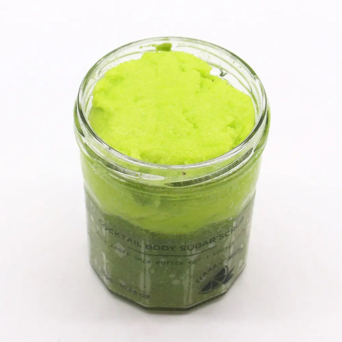 A vibrant lime-green classic mojito sugar body scrub with shea butter in a clear glass jar with an octagonal base