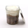 A clear glass jar with a silver lid holding a layered espresso martini sugar body scrub with brown sugar and white cream