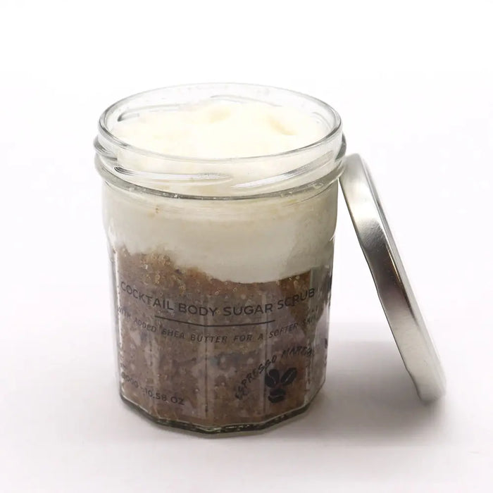 A clear glass jar with a silver lid holding a layered espresso martini sugar body scrub with brown sugar and white cream