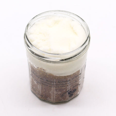 A clear glass jar with a fragranced sugar body scrub layered with brown espresso sugar and white creamy top
