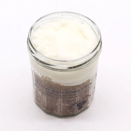 A clear glass jar with a fragranced sugar body scrub layered with brown espresso sugar and white creamy top