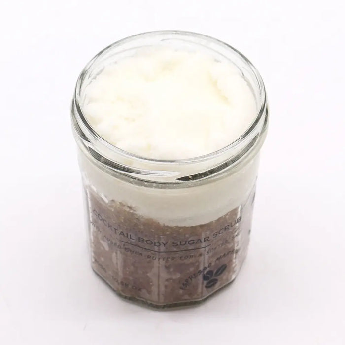 A clear glass jar with a fragranced sugar body scrub layered with brown espresso sugar and white creamy top