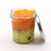 A vibrant orange peach sangria sugar body scrub with shea butter in a clear glass jar with a silver lid