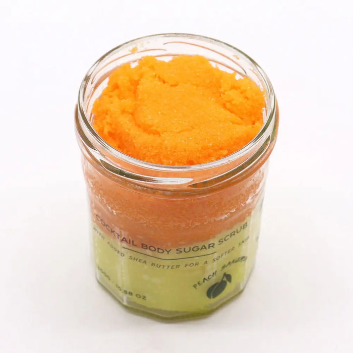 A vibrant orange peach sangria sugar body scrub with shea butter in a clear glass jar and pale green label