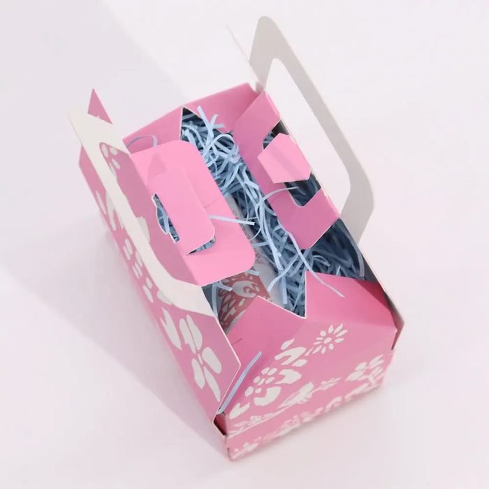 Pink paper cat wellness gift box with white floral cutouts and light blue shredded paper for wellness gift set