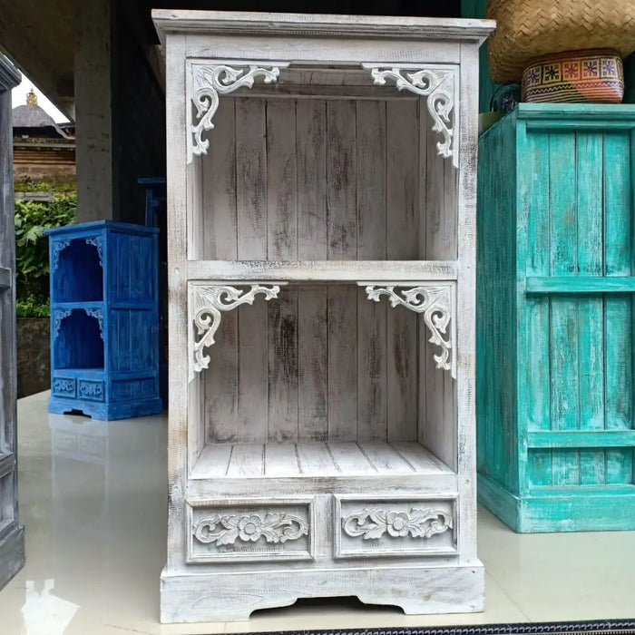 A rustic whitewashed wooden albasia bathroom cabinet with carved floral and scrollwork details on shelves and drawers