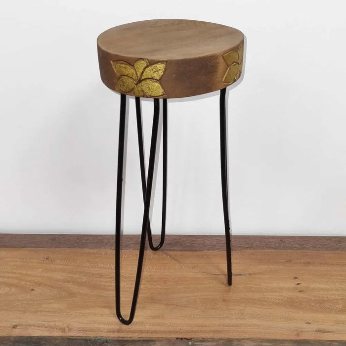 A rustic albasia wood plant stand with a natural round top featuring gold leaf inlay and black metal hairpin legs