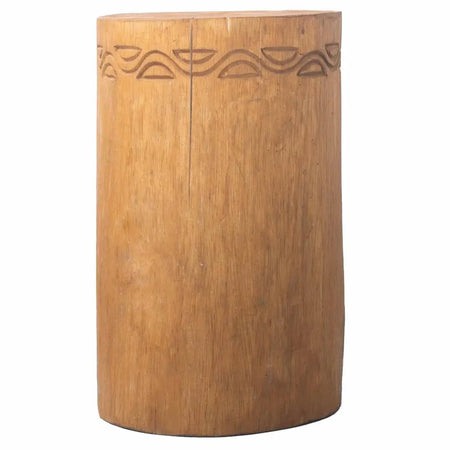 A cylindrical albasia wood tribal plant stand with natural light brown finish and carved wave patterns along top edge