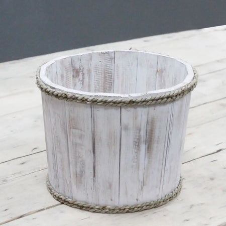 A small albesia wood storage tub with rustic whitewash finish and natural rope trim on top and bottom edges