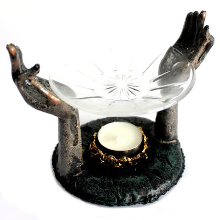 A clear cut glass bowl held by dark bronze hands on a black textured base with gold accents oil burner design