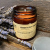 A brown glass jar soy wax aromatherapy candle labeled aphrodisiac with lavender sprigs beside it