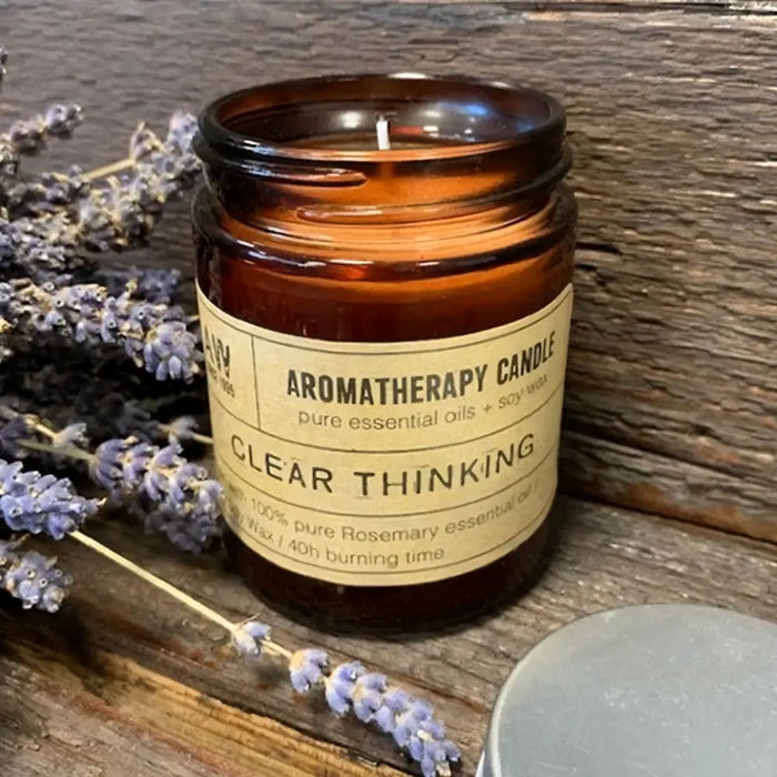An amber glass jar holding a soy wax aromatherapy candle with a beige clear thinking label and a white wick