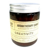 A dark amber glass jar with a silver lid holds a soy wax aromatherapy candle scented for creativity