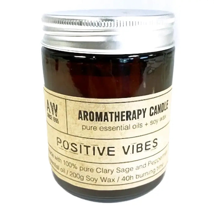 A dark amber glass jar with a silver lid contains a soy wax aromatherapy candle scented with positive vibes