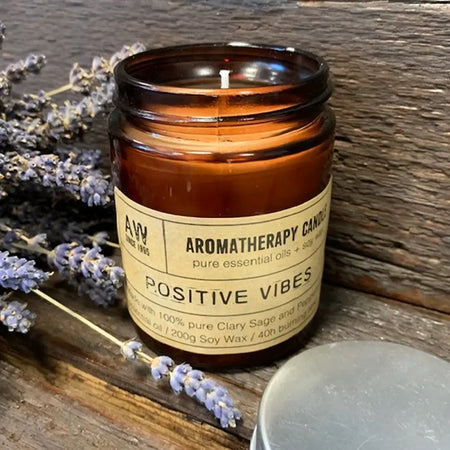 An amber glass jar soy wax aromatherapy candle labeled positive vibes with clary sage and peppermint oils