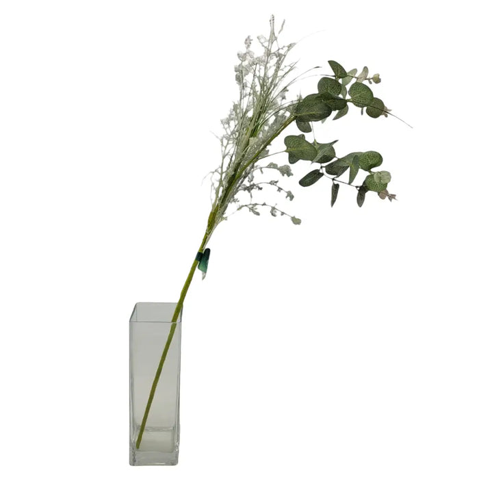 Artificial eucalyptus sprig with slender green leaves and white flowers in a clear rectangular glass vase