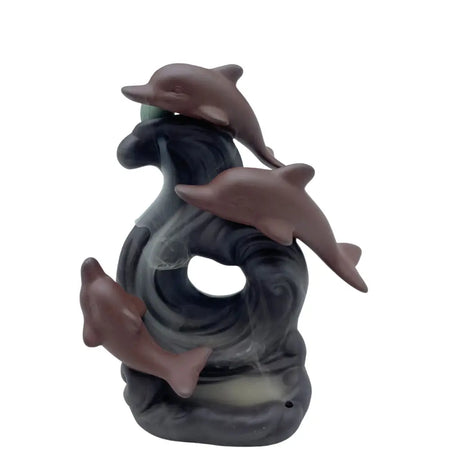 A brownish-gray ceramic backflow incense burner with three dolphins in a swirling ocean design holding a green sphere